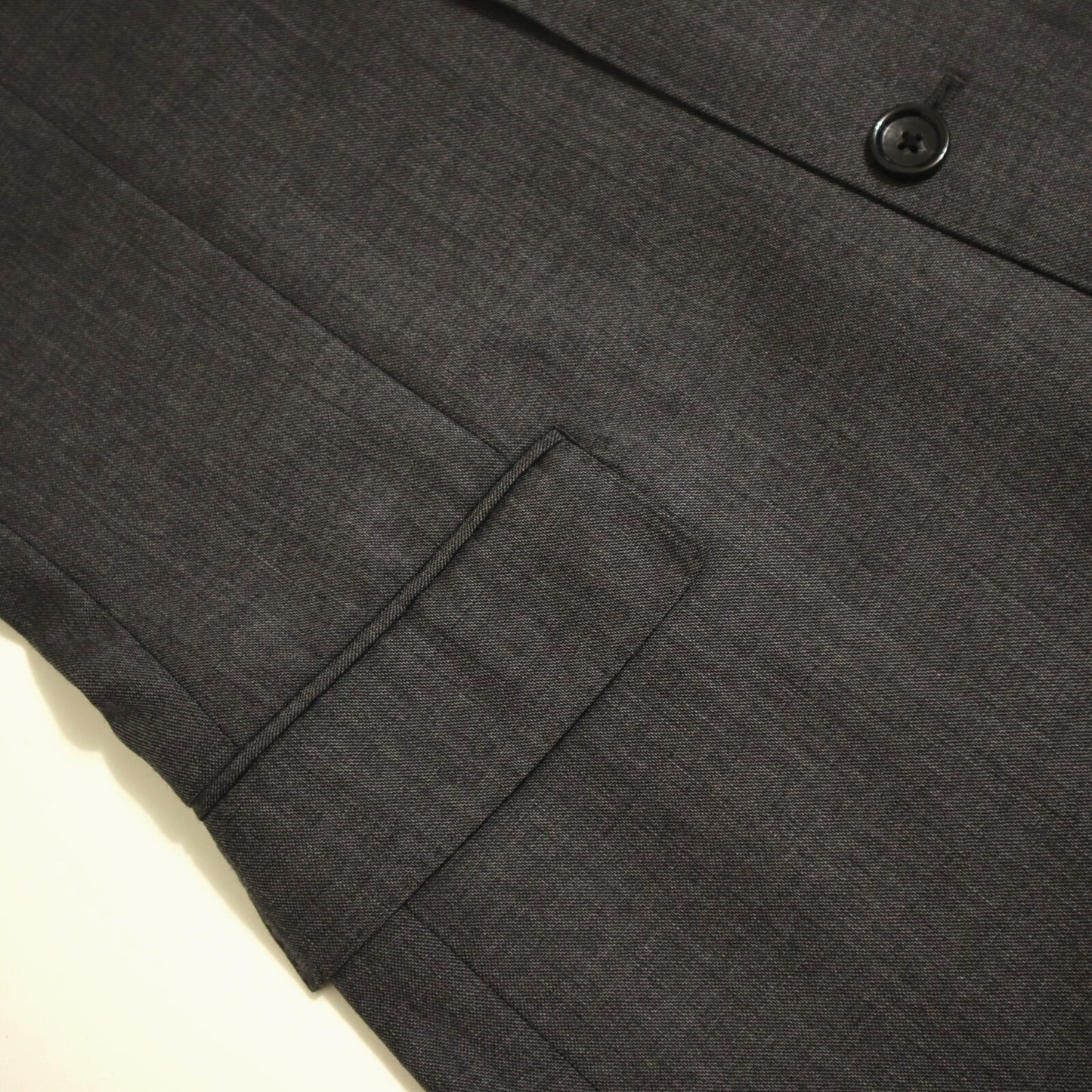 Close-up of a dark gray suit jacket with a button and pocket on a light beige background