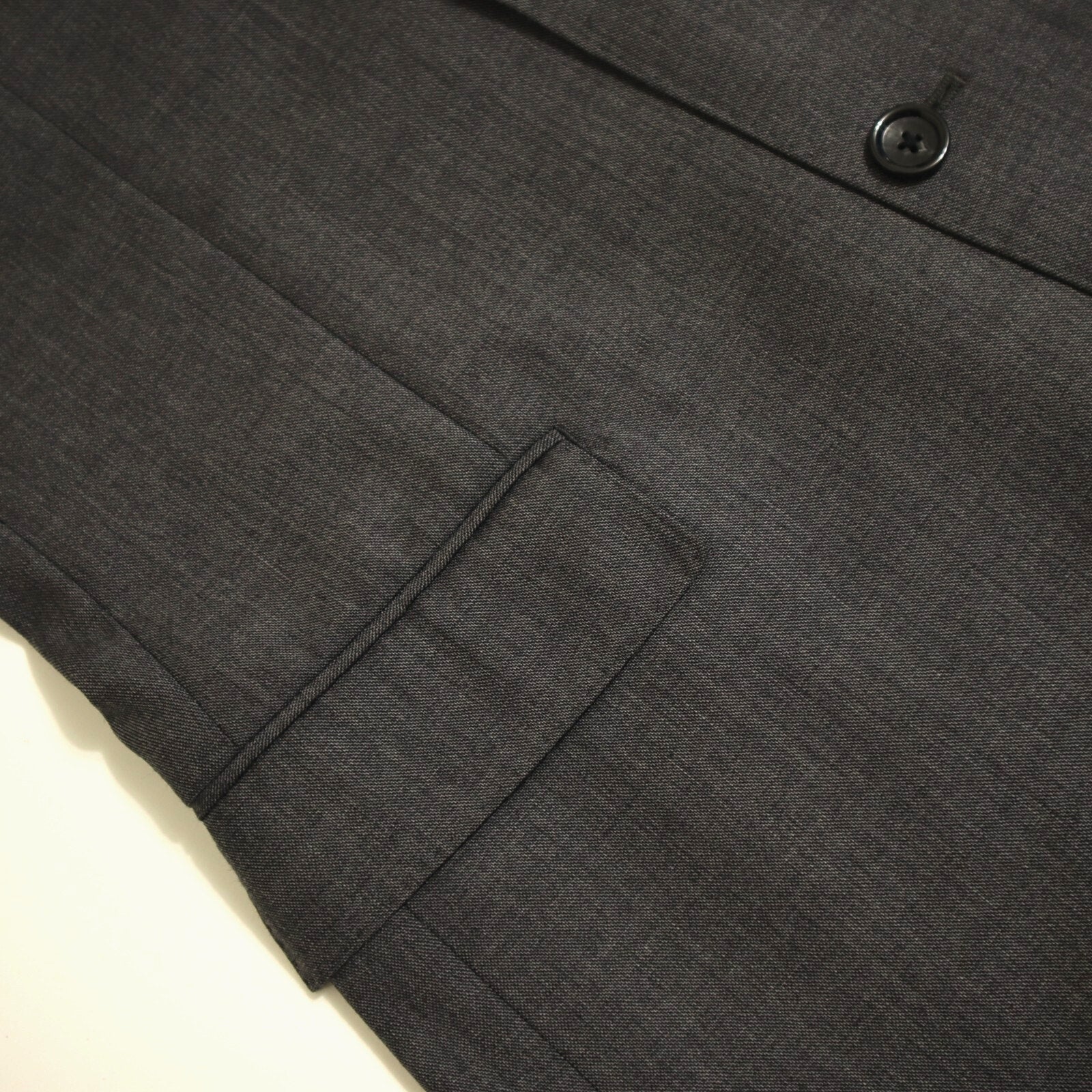 Close-up of a dark gray suit jacket with a button and pocket on a light beige background